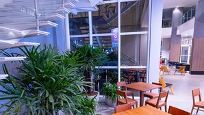 Een moderne, overdekte eetruimte met houten tafels en stoelen, omgeven door potplanten.