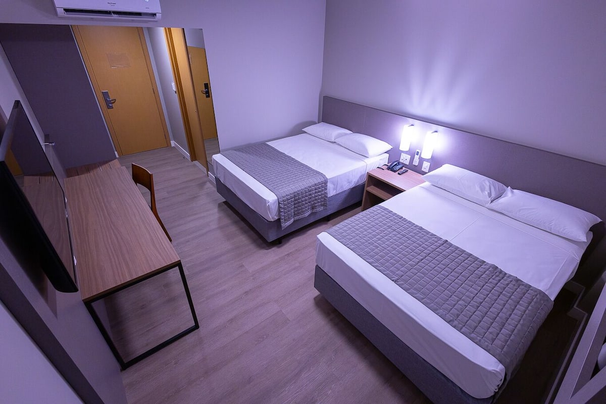 A hotel room with two beds, a desk, and a wardrobe.