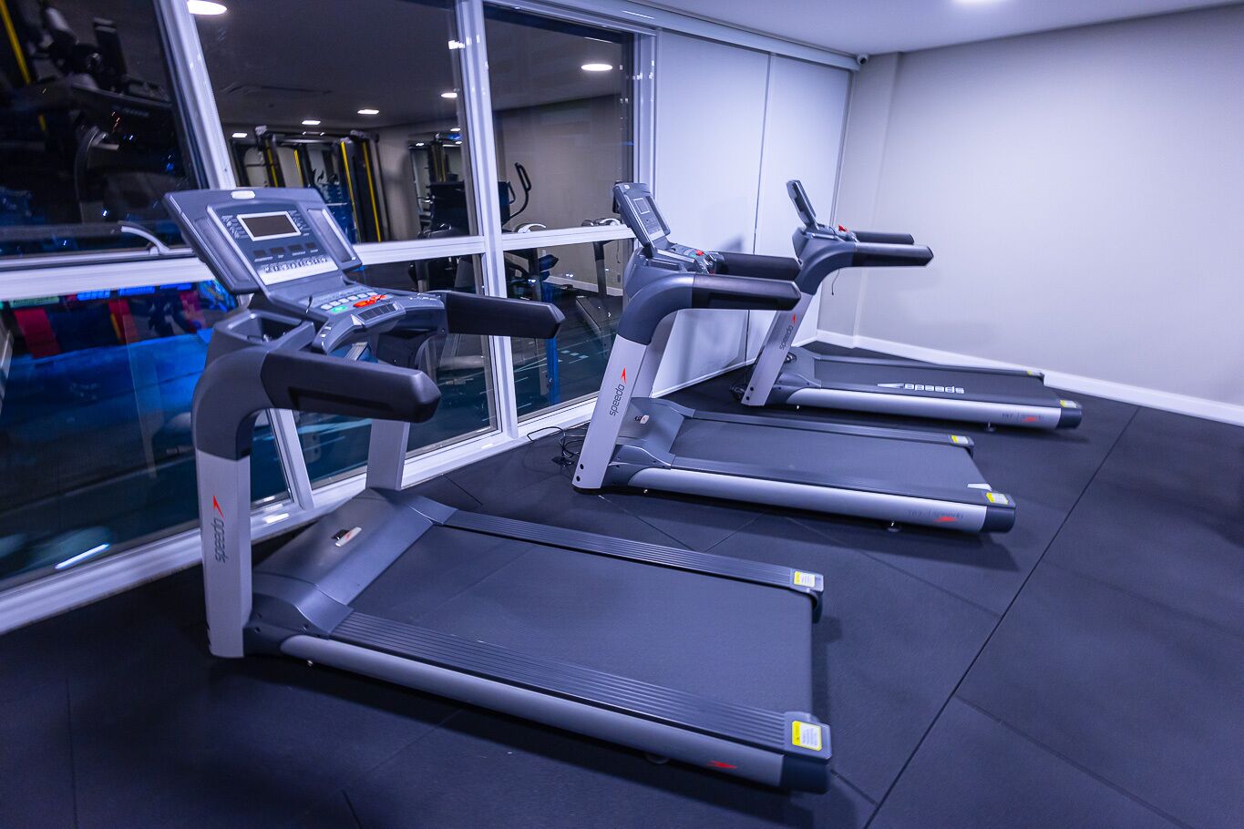 Un gimnasio con cintas de correr, bicicletas estáticas y un espejo grande.