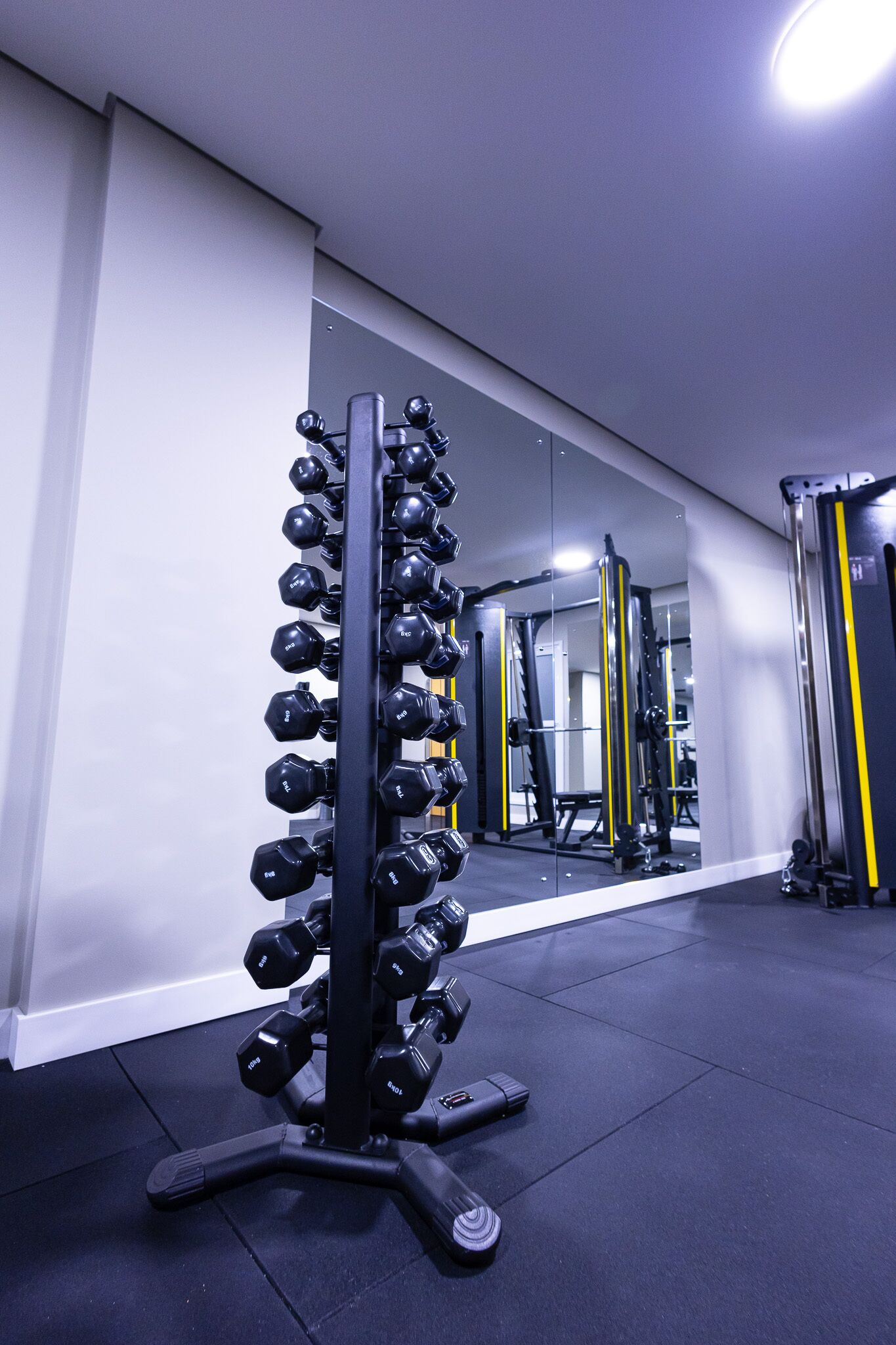 A gym with a rack of dumbbells, weight machines, and a mirror reflecting the equipment.