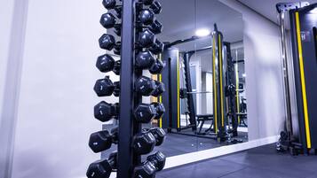 A gym with a rack of dumbbells, weight machines, and a mirror reflecting the equipment.