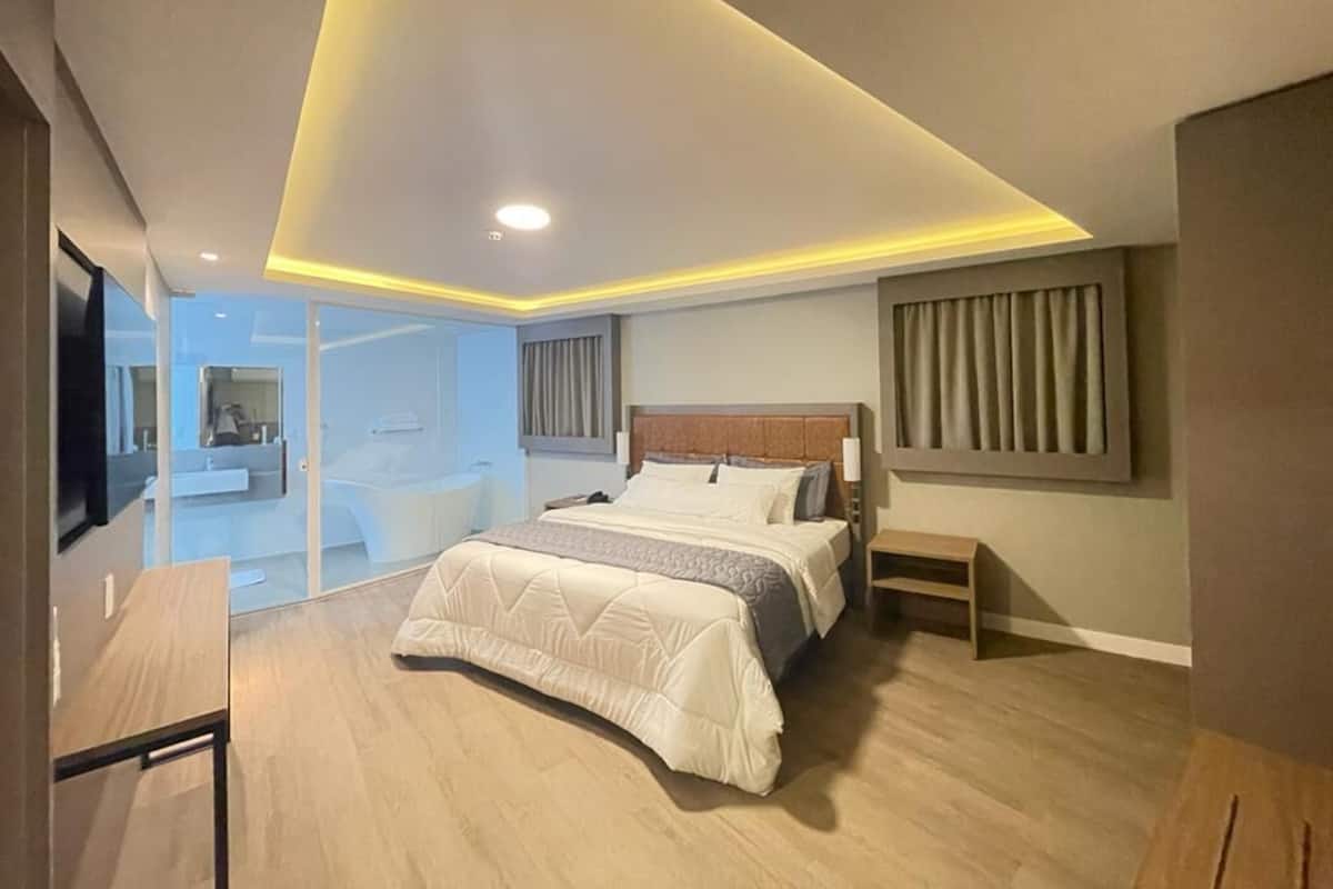 A modern bedroom with a large bed, bedside tables, a nightstand, and a view of a bathroom.