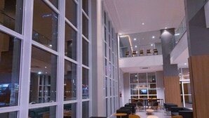 Een ruime lobby met grote ramen, meerdere zithoeken en een hoge plafond.