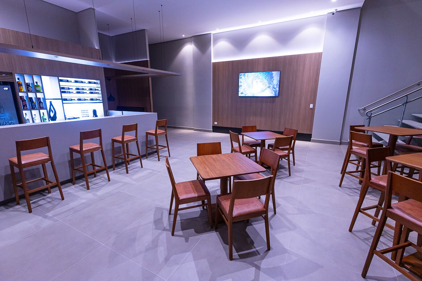 A modern dining area with wooden tables and chairs, a counter with product displays, and a TV on the wall.