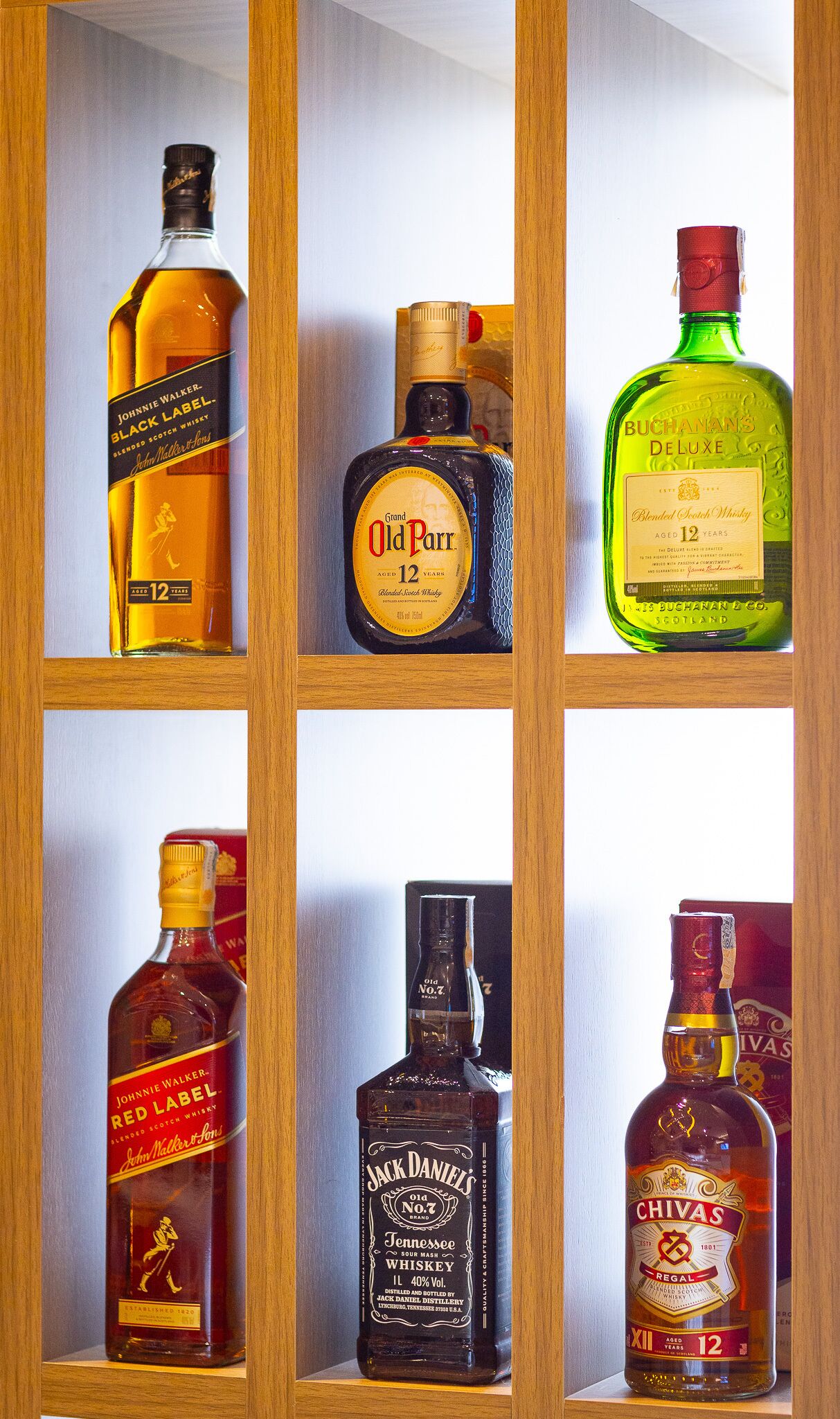 A wooden cabinet with six shelves, each holding a different bottle of whiskey.