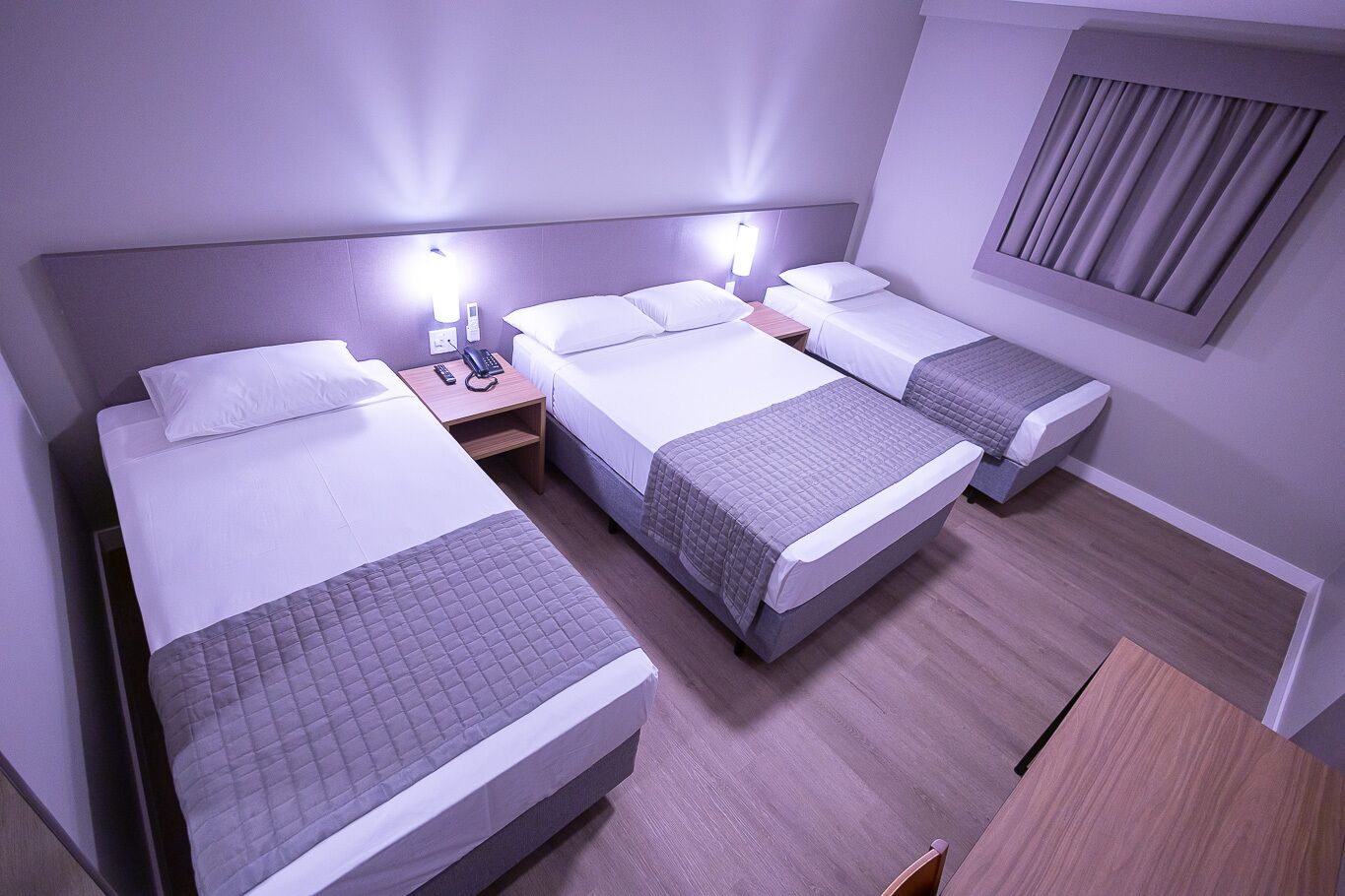 Habitación de hotel con tres camas, un escritorio de madera y una ventana con cortinas.