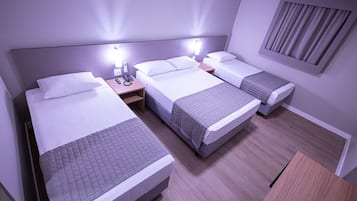 A hotel room with three beds, a wooden desk, and a window with curtains.