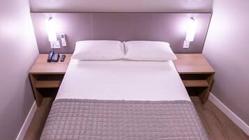 Ein ordentlich bezogenes Bett mit einer gesteppten Decke, zwei Nachttische mit Lampen und ein an der Wand befestigtes Telefon.