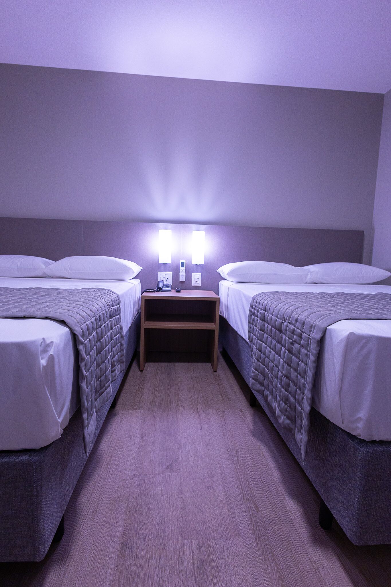 Habitación doble con dos camas, una mesita de noche y una lámpara de pared.
