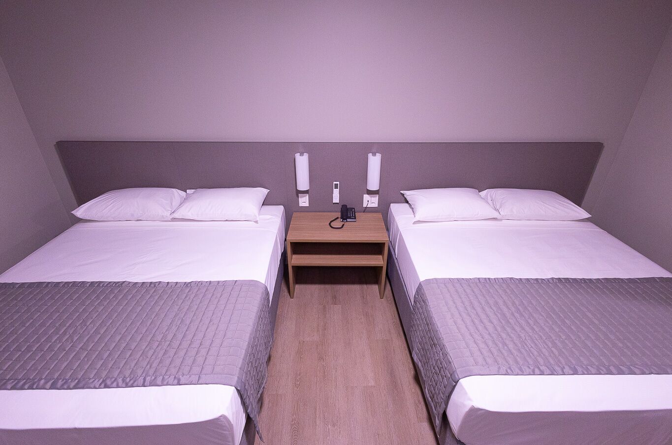 Ein Doppelzimmer mit zwei Betten, einem Holfnachtkästchen und einem Telefon.