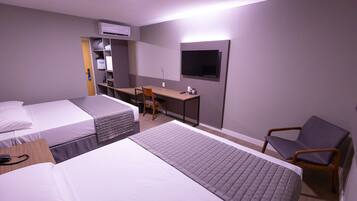 A hotel room with two beds, a desk, a chair, a TV, and an air conditioning unit.