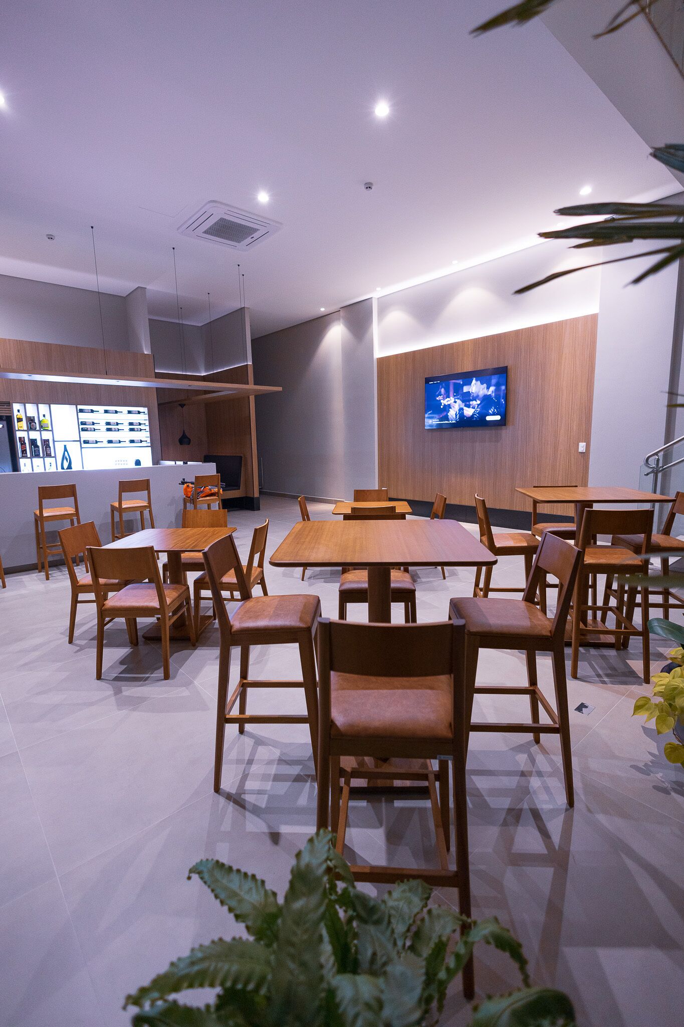 Un área de comedor moderna con mesas y sillas de madera, un televisor de pantalla plana en la pared y una barra con un menú a la vista.