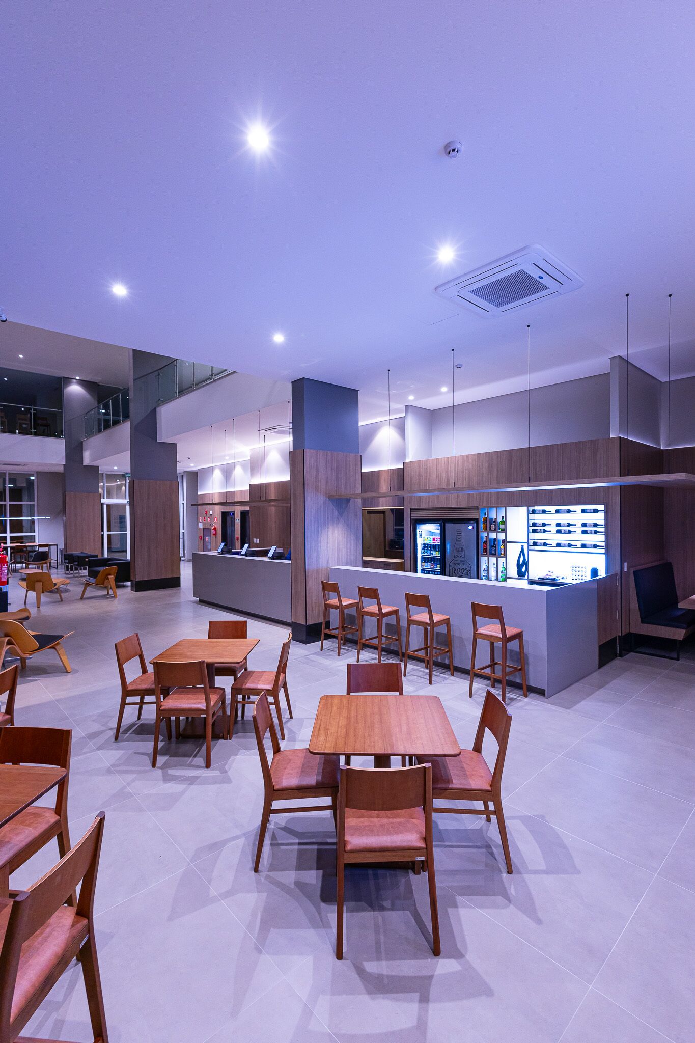 Un restaurante moderno con mesas y sillas de madera, una zona de bar y un techo alto con iluminación empotrada.