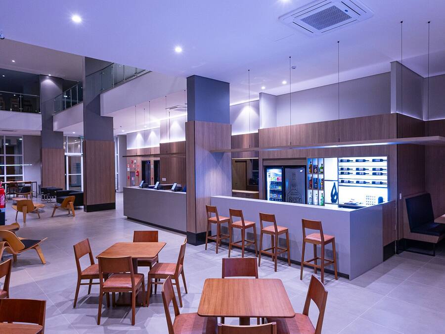 Un restaurante moderno con mesas y sillas de madera, una zona de bar y un techo alto con iluminación empotrada.