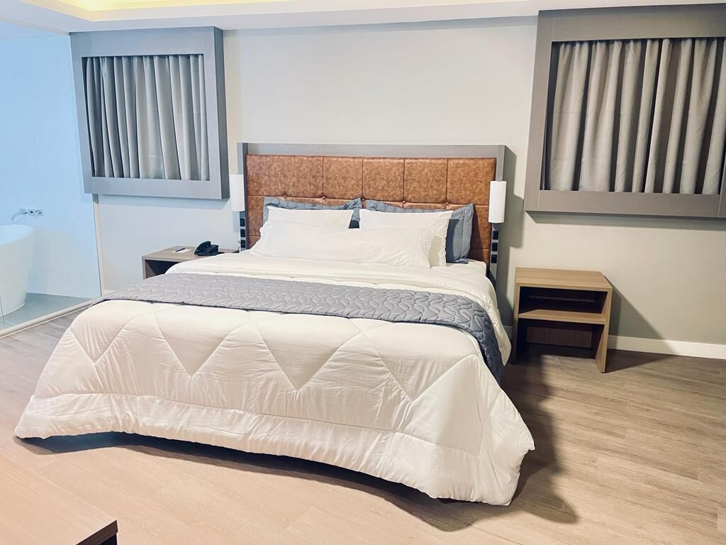 Una habitación de hotel moderna con una cama grande, cabecero de madera, mesitas de noche y cortinas.