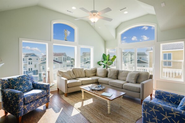 Relax in this inviting living room with a high ceiling, ceiling fan, and large windows offering views of the surrounding neighborhood.