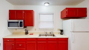 Una cocina compacta con armarios rojos, un microondas, un lavamanos y un refrigerador.