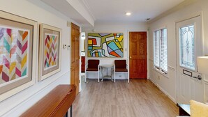Un pasillo con obras de arte enmarcadas, un comedor con mesa y sillas, y un cuadro abstracto grande en la pared.