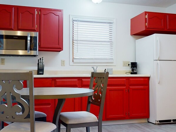 A kitchen with red cabinets, a white refrigerator, a microwave, and a window with blinds.