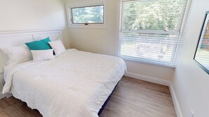 Een slaapkamer met een groot bed, een raam met zonwering en uitzicht op bomen.