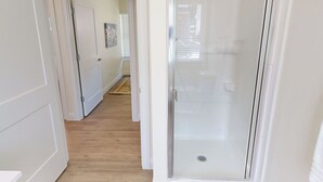 Een hal met een douchecabine van glas, houten vloeren en een deur naar een andere kamer.
