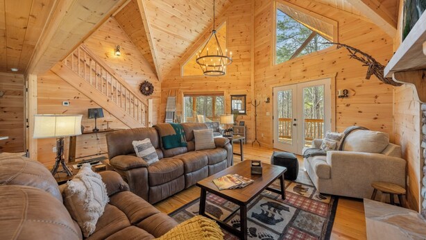A cozy log cabin interior with a living room, fireplace, and large windows.