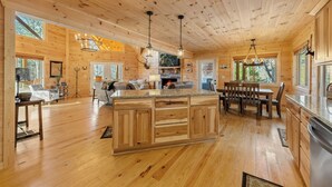 A spacious wooden cabin interior with a large kitchen island, dining area, and a cozy seating space.