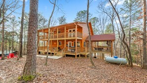 A multi-story wooden cabin with a balcony, surrounded by trees.
