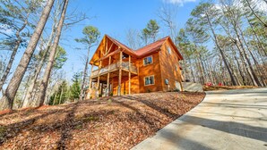 A log cabin with a porch, surrounded by tall trees and a clear sky.