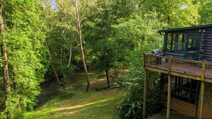 Une cabane dotée d’une terrasse donnant sur une zone boisée et un ruisseau.