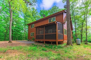 A cabin with a large porch, surrounded by trees.