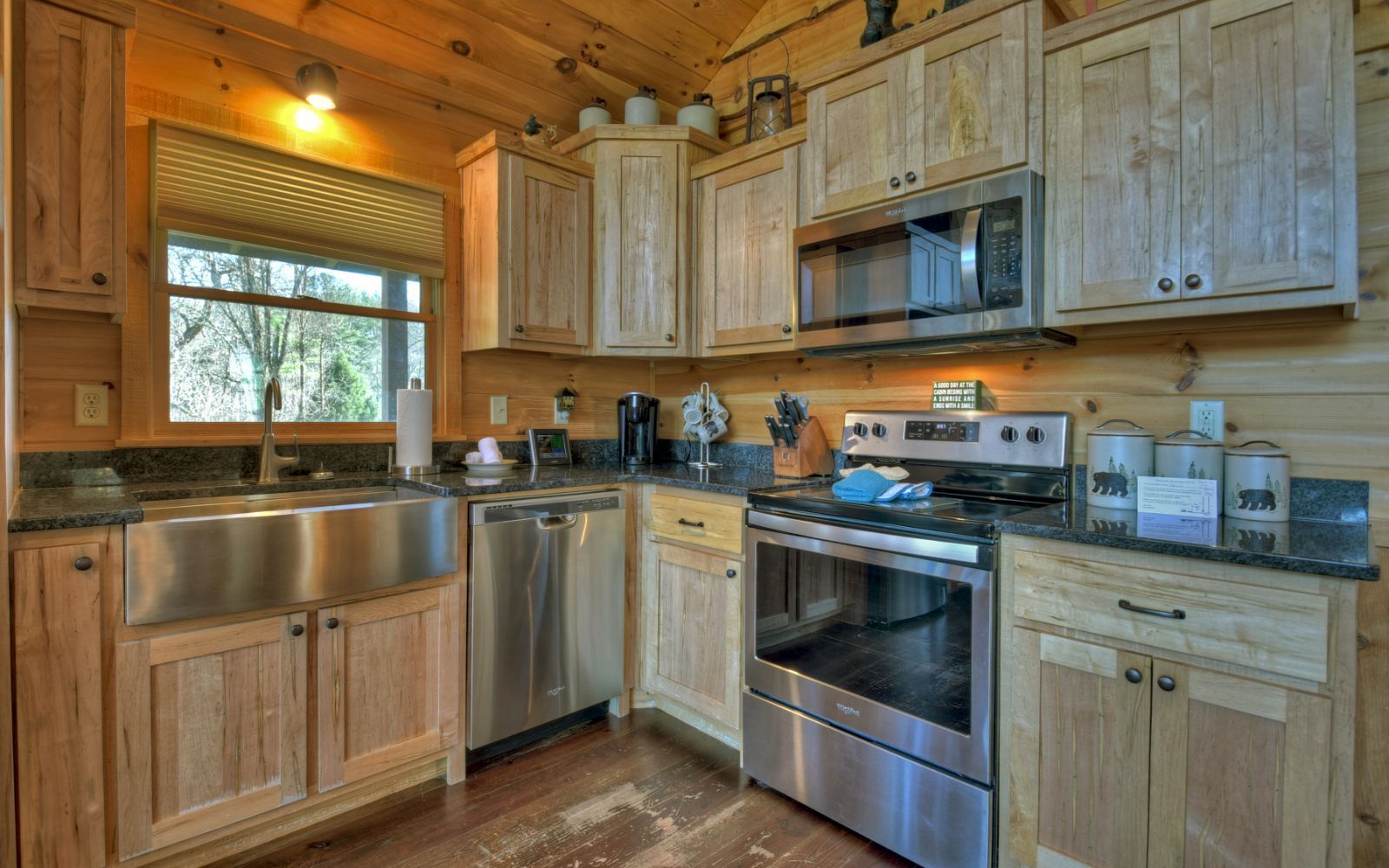 A wooden cabin-style kitchen with a stainless steel sink, dishwasher, microwave, stove, and oven.