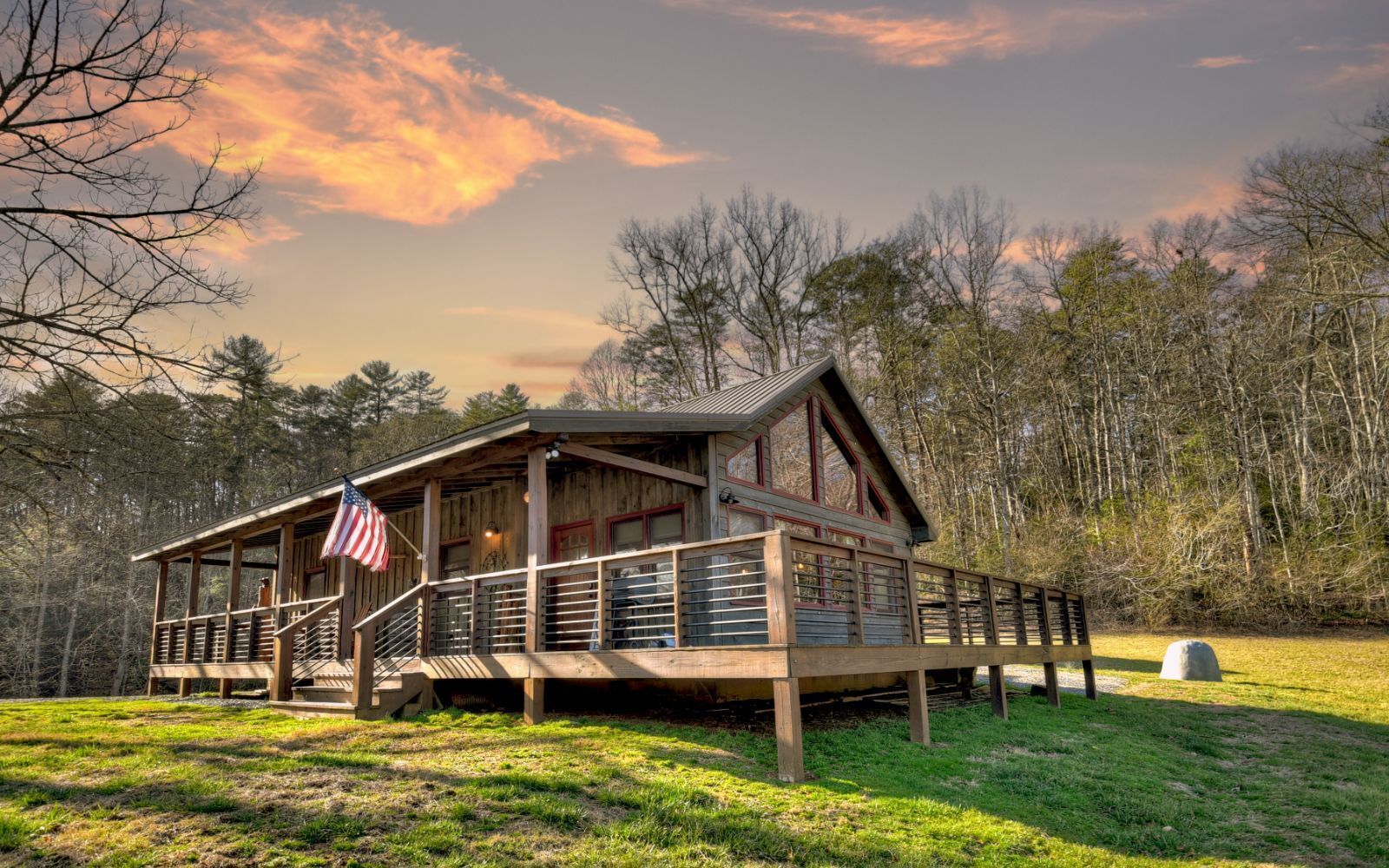 A wooden cabin with a porch and an American flag, surrounded by trees.