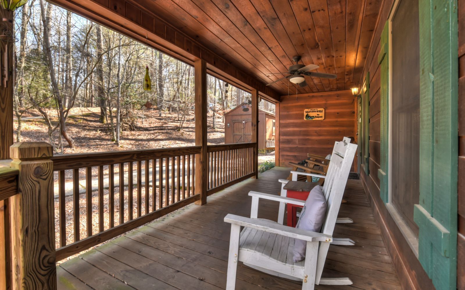 A wooden cabin with a porch, wooden deck, and a view of the forest.