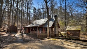 Eine rustikale Holzhütte mit Veranda, einem separaten Schuppen und einer kleinen Holzkonstruktion.