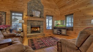 Ein gemütliches Blockhaus-Interieur mit Kamin aus Stein, Ledersofas, einem Flachbildfernseher und einer Holz-Unterhaltungsanlage.