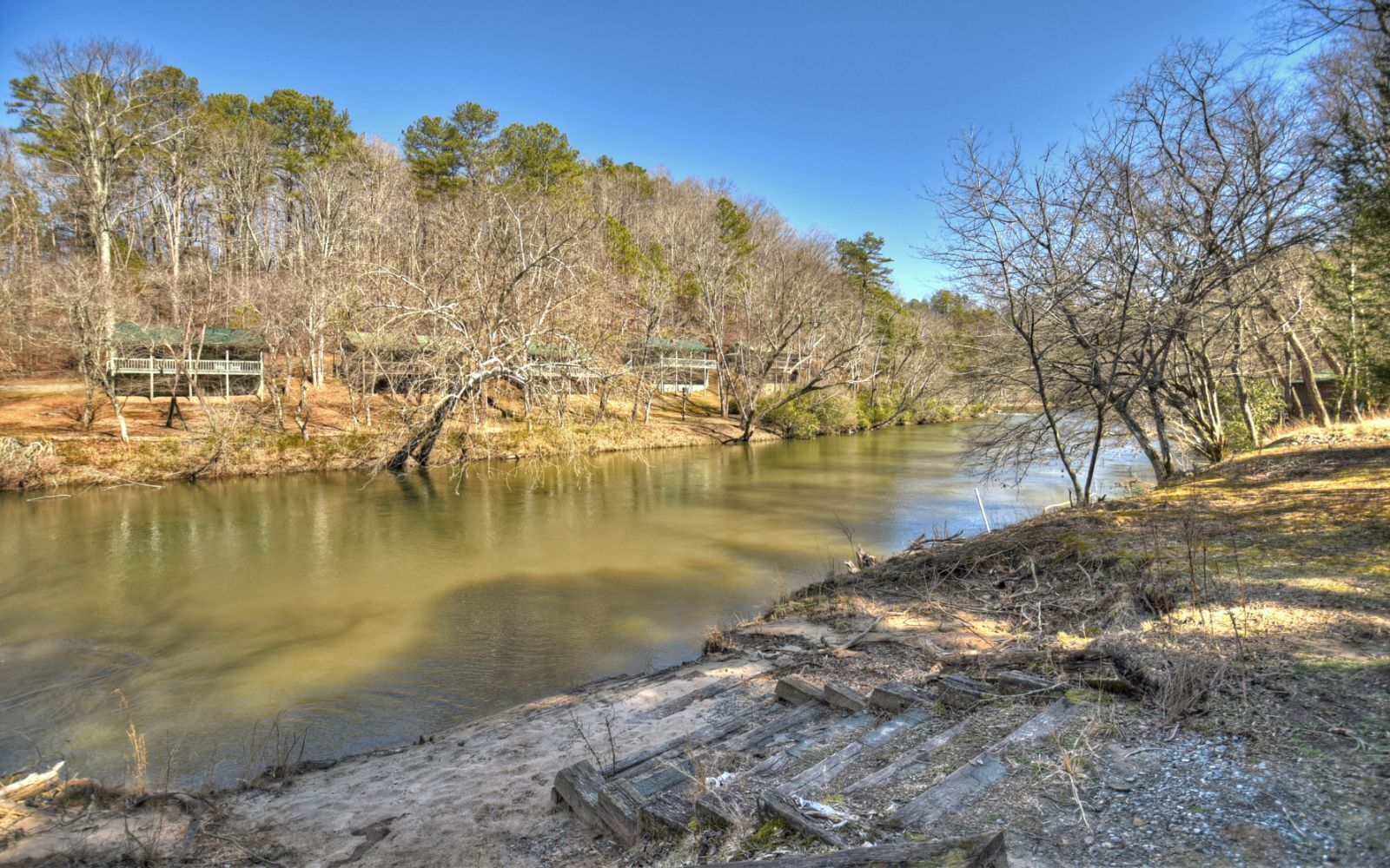 A riverbank with a wooden bench and a wooden fence.