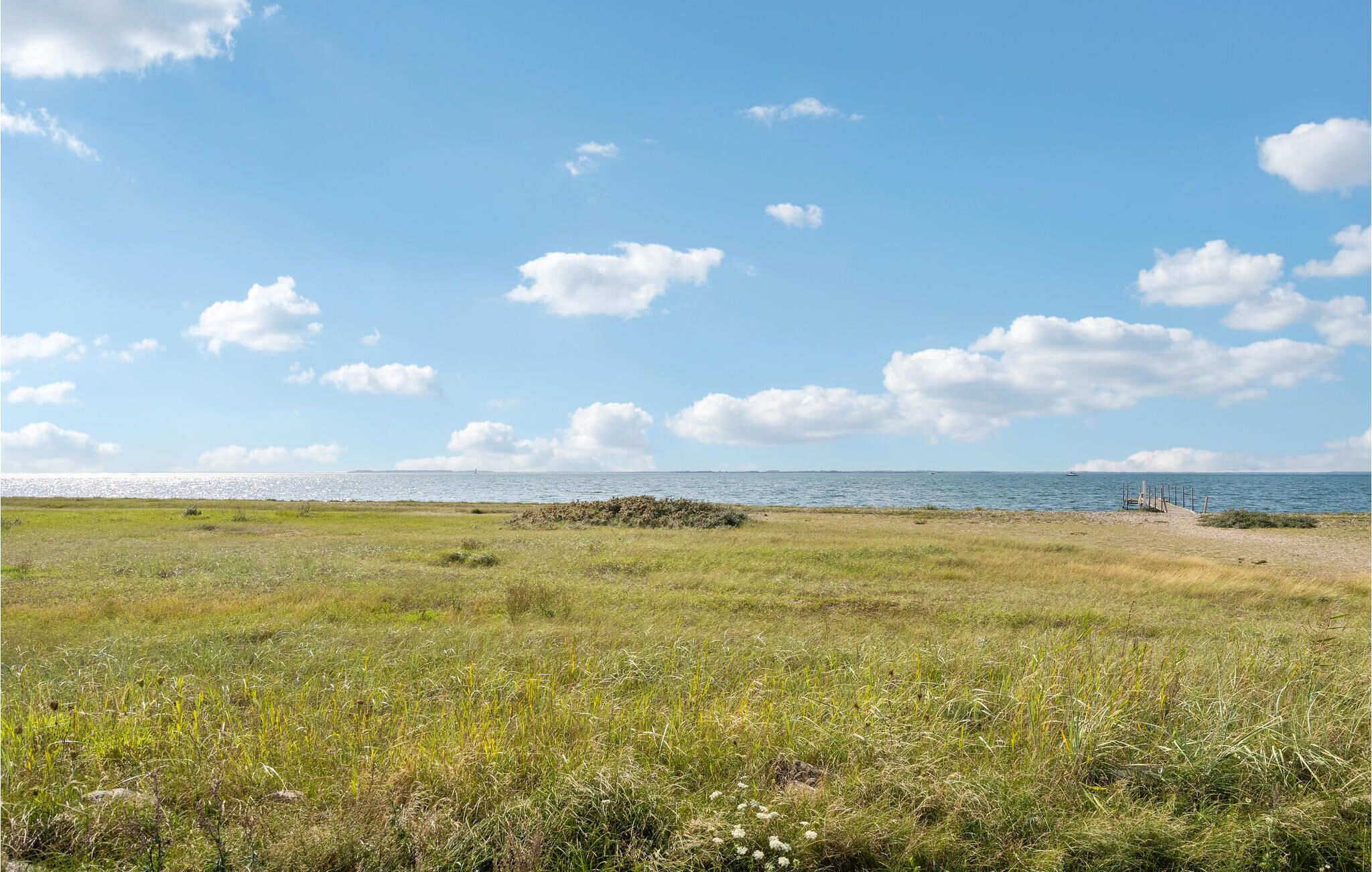 Un paysage côtier avec un premier plan herbeux, un ciel dégagé et une vue lointaine sur la mer.