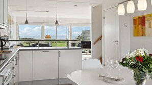 A modern kitchen with a view of the sea, a dining area with a table set for two, and a painting on the wall. - Nice home in Assens with house sea view (Assens)