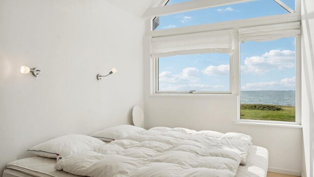 A bedroom with a bed, two wall-mounted lights, and a window with a view of the sea. - Nice home in Assens with house sea view (Assens)
