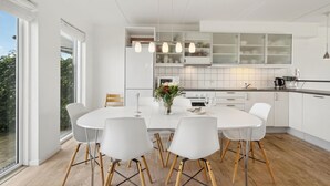 A modern kitchen with white cabinetry, a round dining table with white chairs, and a view of greenery outside. - Nice home in Assens with house sea view (Assens)