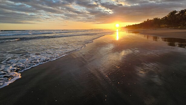 Ein Strand mit Sonnenuntergang, Wellen und blauem Himmel.