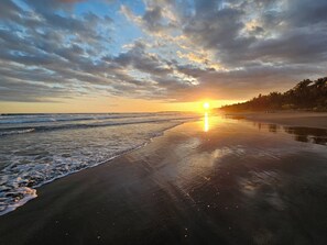 Una playa con un atardecer, olas y cielo despejado.
