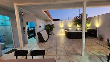 A covered outdoor patio with a hot tub, seating area, and a glass-enclosed shower room.