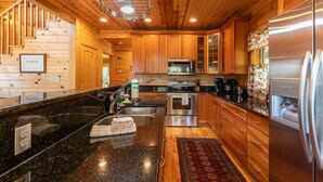 A modern kitchen with wooden cabinets, stainless steel appliances, a granite countertop, and a red patterned rug. - Morris Cabin- Cedar log cabin with hot tub, dog friendly, mountain views (Boone)