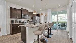 Une cuisine moderne avec des meubles en bois foncé, des appareils électroménagers en acier inoxydable et un îlot central doté de tabourets de bar.