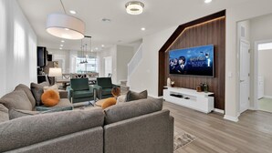 Un salon moderne avec un canapé d’angle, un téléviseur à écran plat et un escalier menant à un autre niveau.