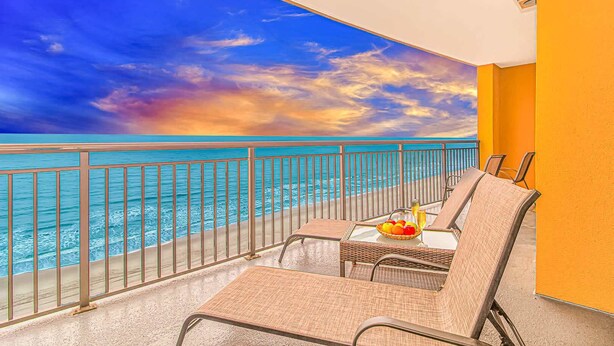 Een balkon met uitzicht op de oceaan, een tafel met een schaal fruit en twee stoelen.