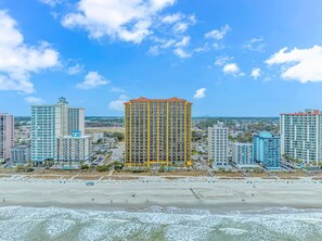 A coastal cityscape with high-rise buildings, a beach, and a clear sky.
