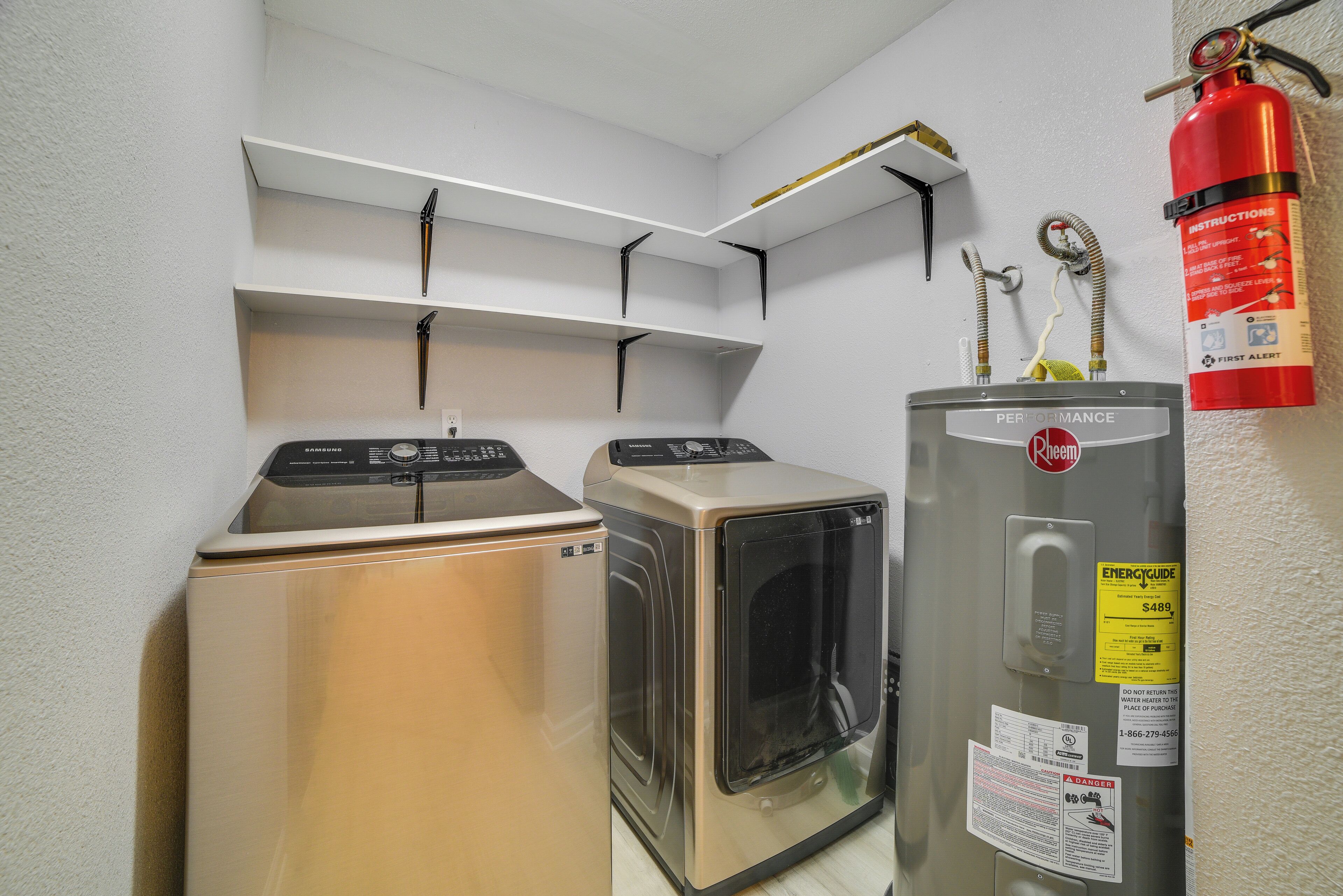 A laundry area with two washers and a dryer, a fire extinguisher, and a water heater.